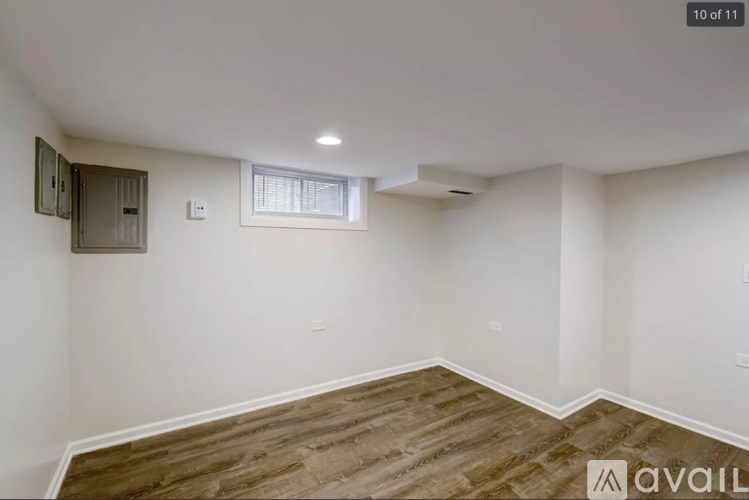 A room with wooden flooring and white walls, with a window and a small cabinet.