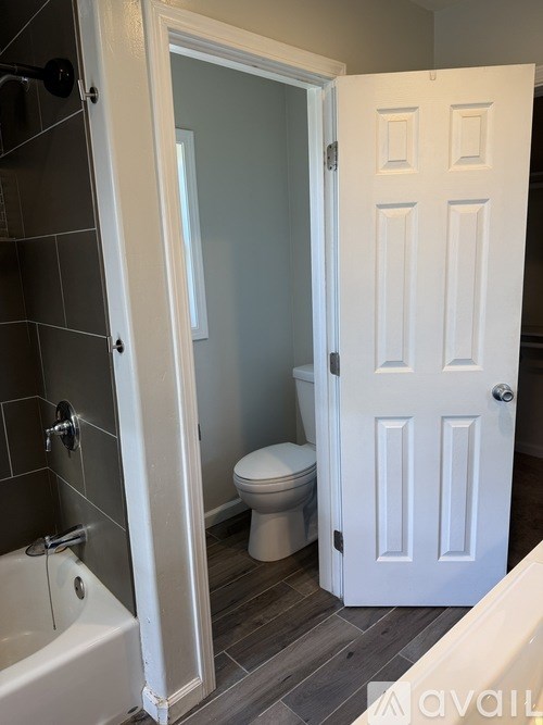A white door is open to a bathroom with a toilet and a tub.