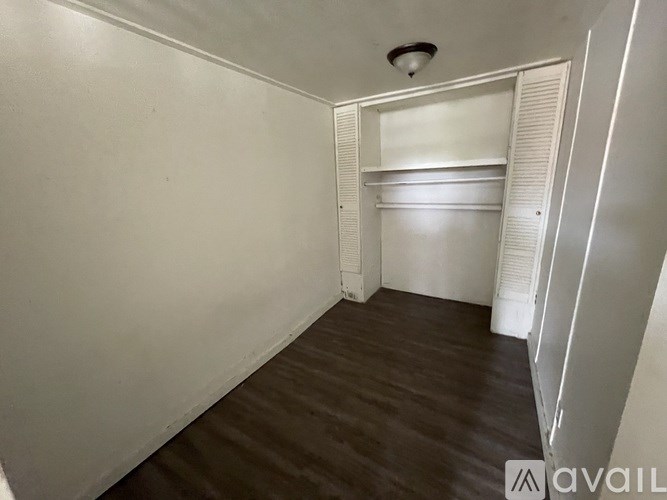 A room with a wooden floor and white walls, featuring a built-in shelf and a ceiling light fixture.