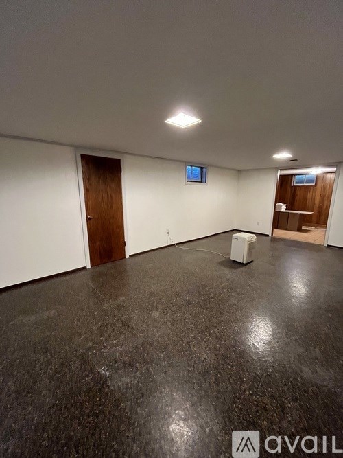 A room with a dark floor and white walls, with a wooden door on the left and a small window on the right.