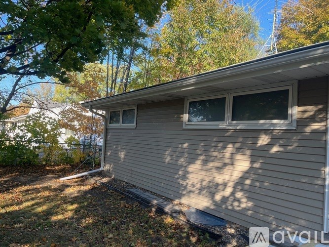 A house with a grey siding and a white window is surrounded by trees.