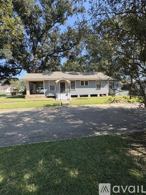 A house with a grey roof and a white fence is surrounded by green grass and trees.