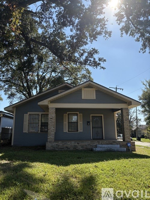 A house with a blue exterior and a white roof is surrounded by green grass and trees.