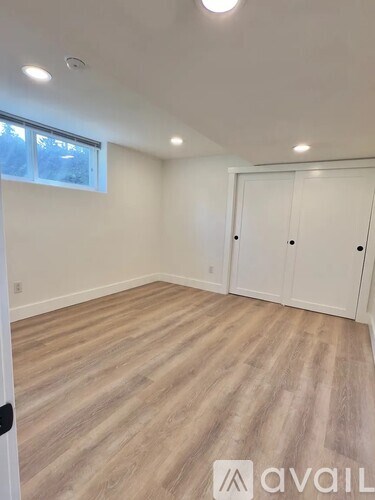 A room with wooden flooring and white walls, with a window and a door.