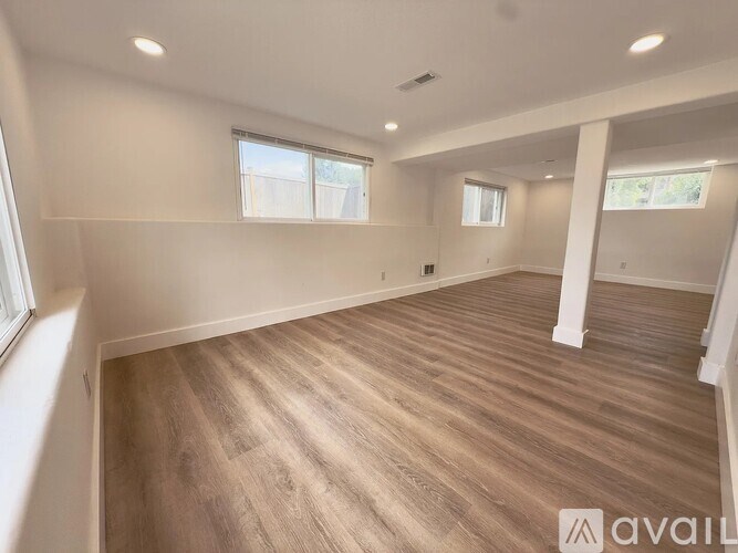 A spacious room with wooden flooring and white walls.