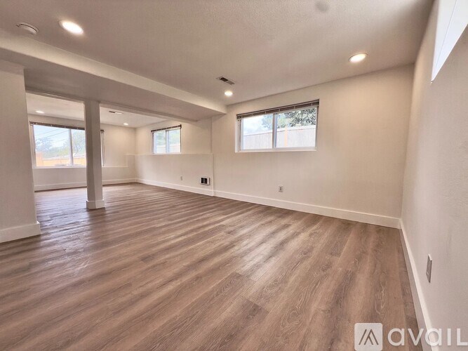A spacious room with wooden flooring and two windows.