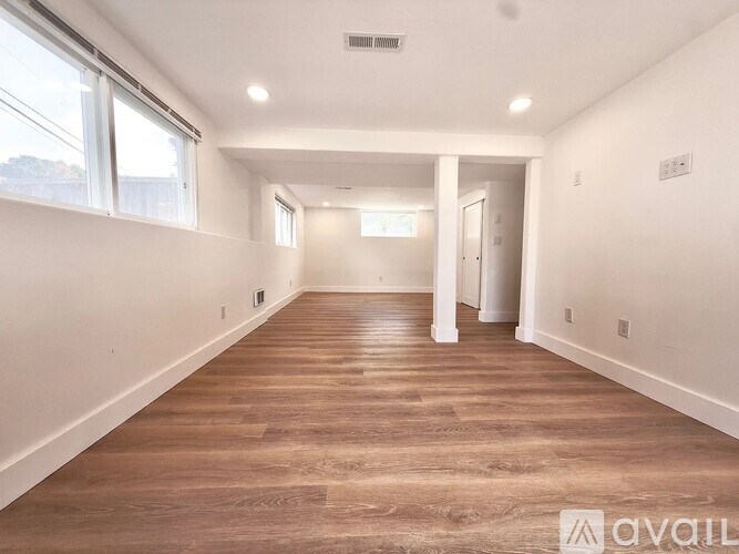 A spacious room with wooden flooring and white walls.