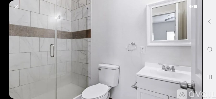 A white toilet sits in a bathroom with a marble tile shower.