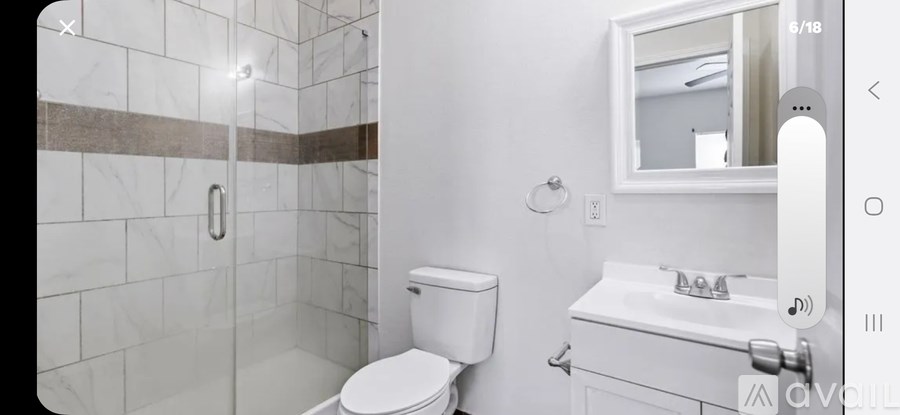 A white toilet sits in a bathroom with a marble tile shower.