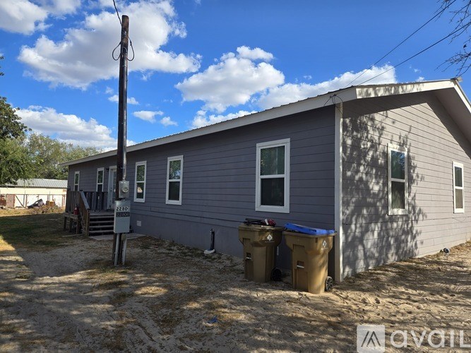 A grey house with a blue roof and a brown trash can.