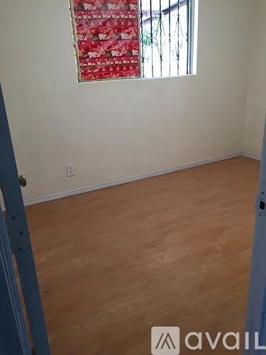 A room with wooden flooring and a window with a red curtain.
