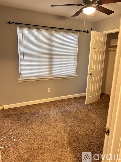 A room with a carpeted floor, a ceiling fan, and a window with blinds.
