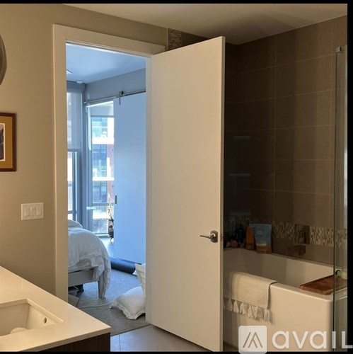 A bathroom with a towel hanging on the tub and a bedroom visible through the open door.