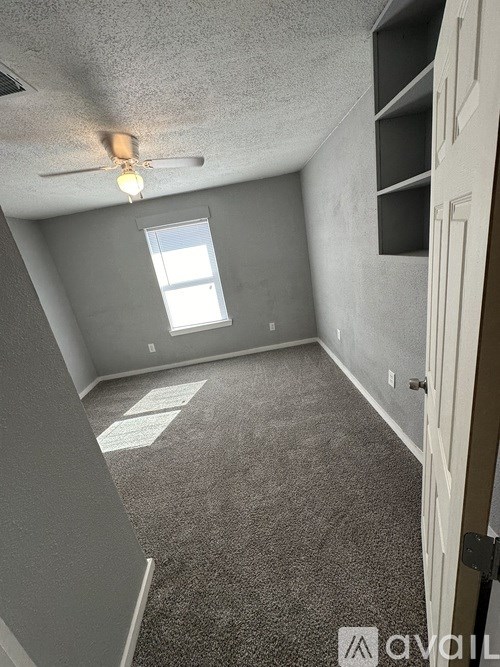 A room with a carpeted floor, a ceiling fan, and a window.