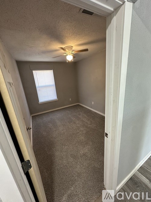 A small, empty room with a window and carpeted floor.