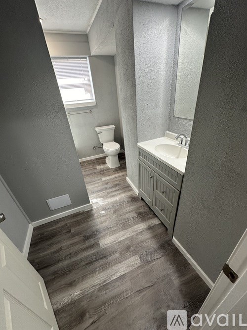 A bathroom with a toilet, sink, and wooden floors.