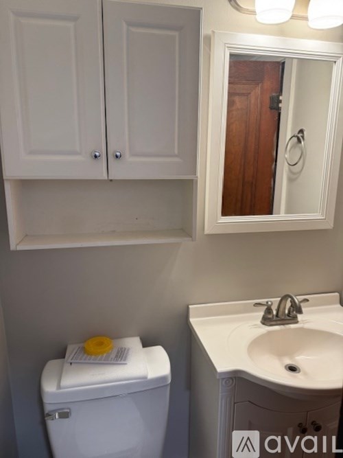 A white toilet with a yellow lid is in a bathroom with a white sink and a mirror.