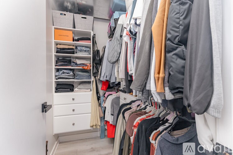 A white closet with clothes hanging and folded in a drawer.