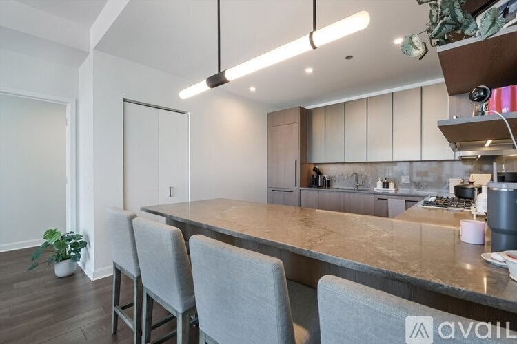A modern kitchen with a long island and grey chairs.