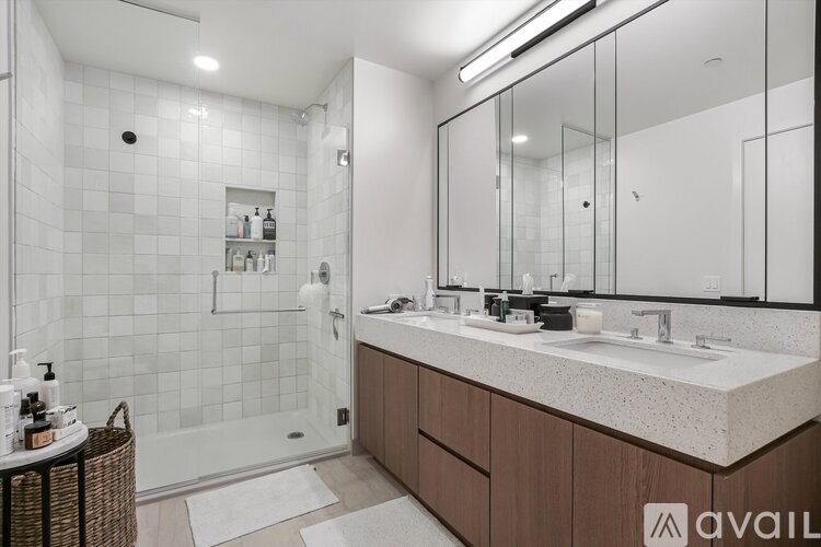 A bathroom with a white tiled shower and a large mirror above a double sink vanity.