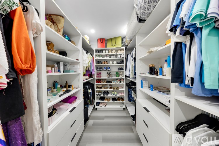A walk-in closet with white shelves and drawers, filled with clothes and shoes.