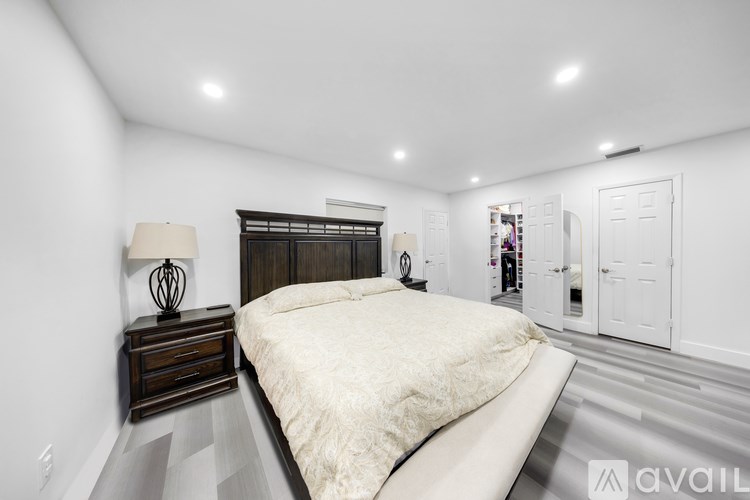 A bedroom with a large bed, a wooden nightstand with a lamp, and a white wall.