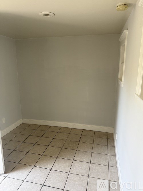 A room with a white tile floor and a white wall with a wooden cabinet and drawers.