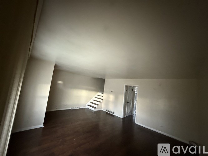 A room with wooden floors and white walls, with a staircase leading to another room.