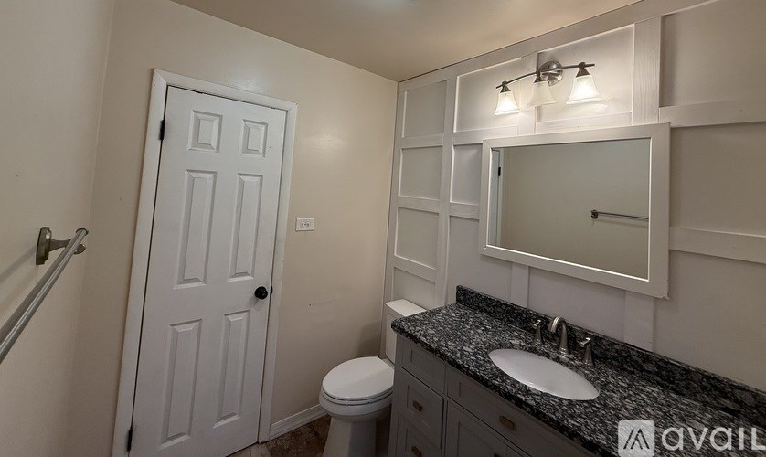 A bathroom with a white door, a black granite countertop, and a mirror above the sink.