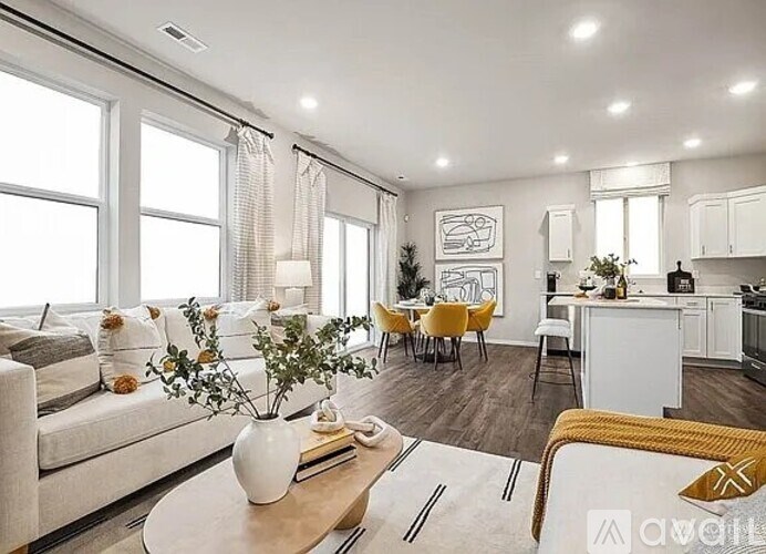 A well-lit, modern living room with a dining area and kitchen in the background.