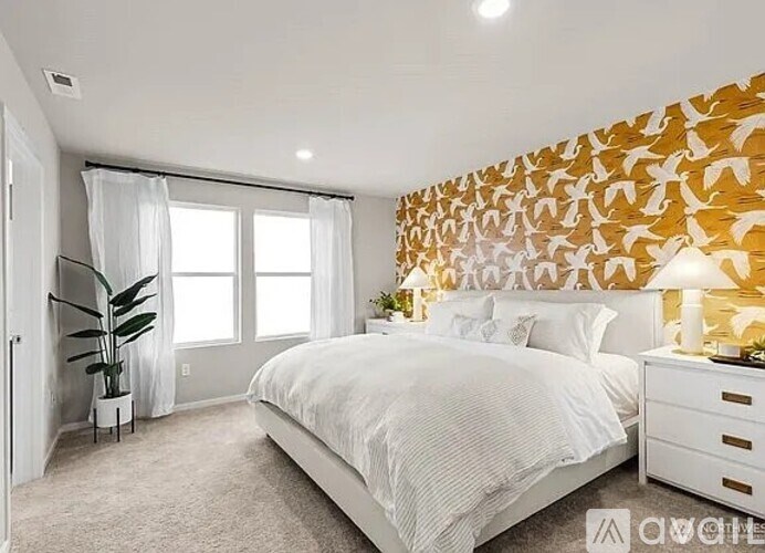 A bedroom with a white bed, a white dresser, and a wall with a leafy pattern.