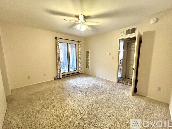 A spacious room with a carpeted floor, a ceiling fan, and a sliding glass door leading to a balcony.