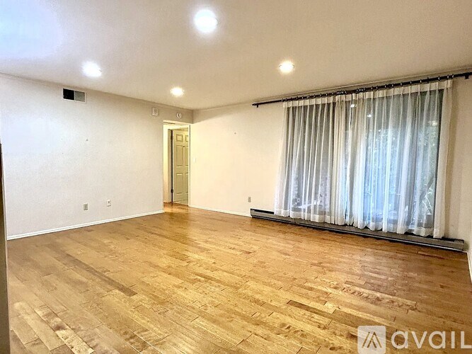A room with wooden flooring and a window with curtains.