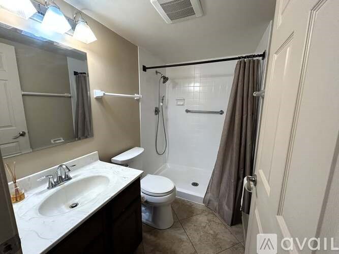 A bathroom with a white sink, toilet, and a shower with a grey curtain.