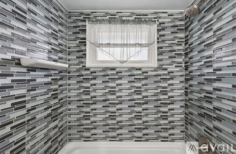 A bathroom with a grey tiled wall and a window.