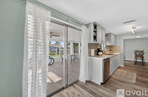 A kitchen with a white curtain and wooden floors.