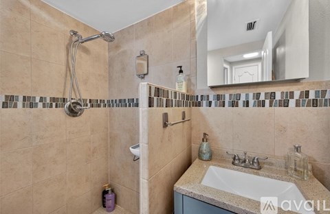A bathroom with a beige tiled shower and sink area.