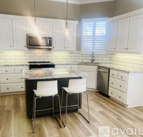 A kitchen with white cabinets and a black island with two chairs.