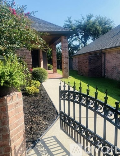A black wrought iron fence with a brick wall and a house in the background.