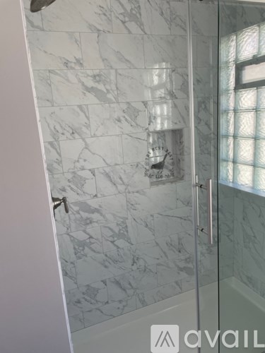 A bathroom with a marble tile wall and a glass shower door.