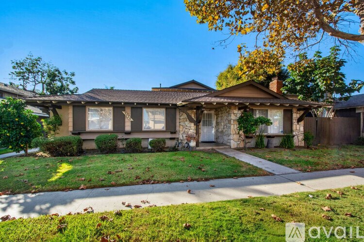 A house with a brown roof and a white door is surrounded by green grass and trees.