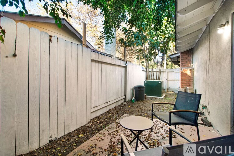 A patio with a chair and table is surrounded by a white fence.