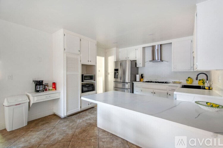 A kitchen with white cabinets and appliances, a marble countertop, and a tiled floor.