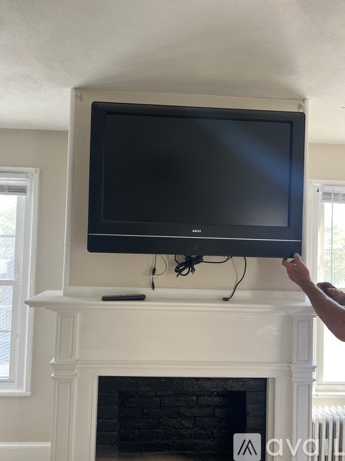 A person is holding a flat screen TV above a fireplace.