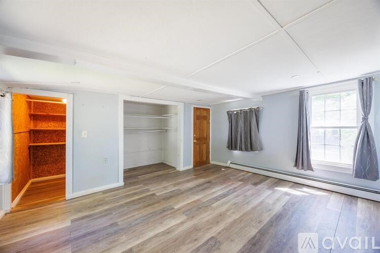 A spacious room with wooden flooring and a large window with curtains.