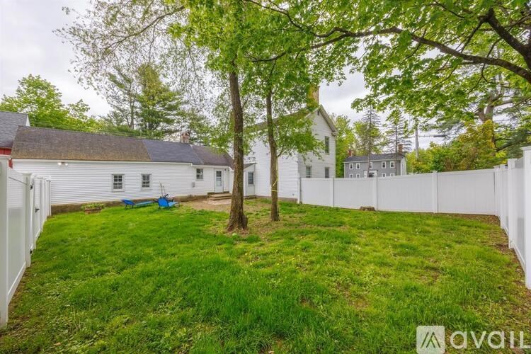 A white fence encloses a green yard with a tree and a house in the background.