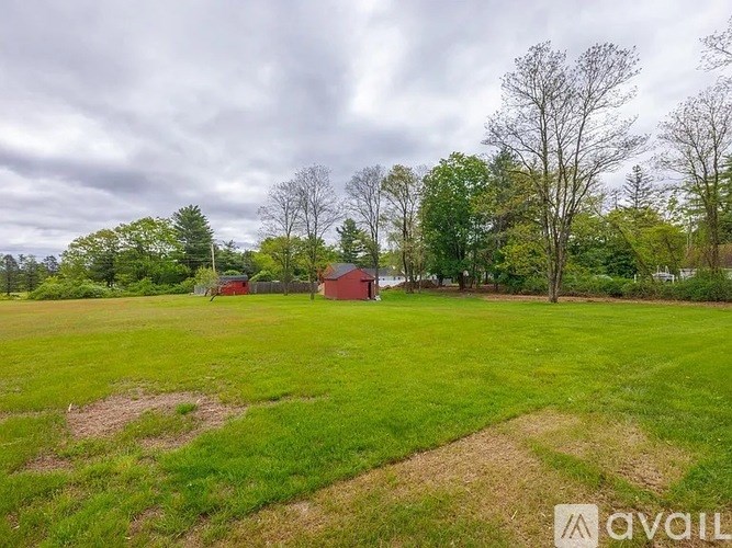 A grassy field with a red barn and trees in the background.