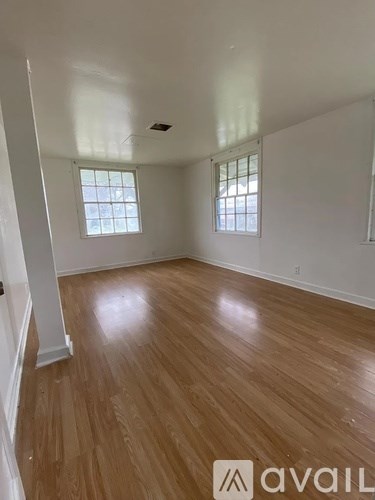 A room with wooden flooring and two windows.