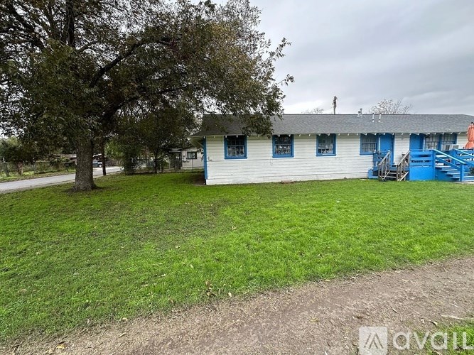 A white house with a blue door and windows is surrounded by a green lawn.