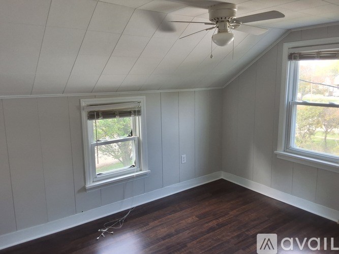 A room with a ceiling fan and two windows.